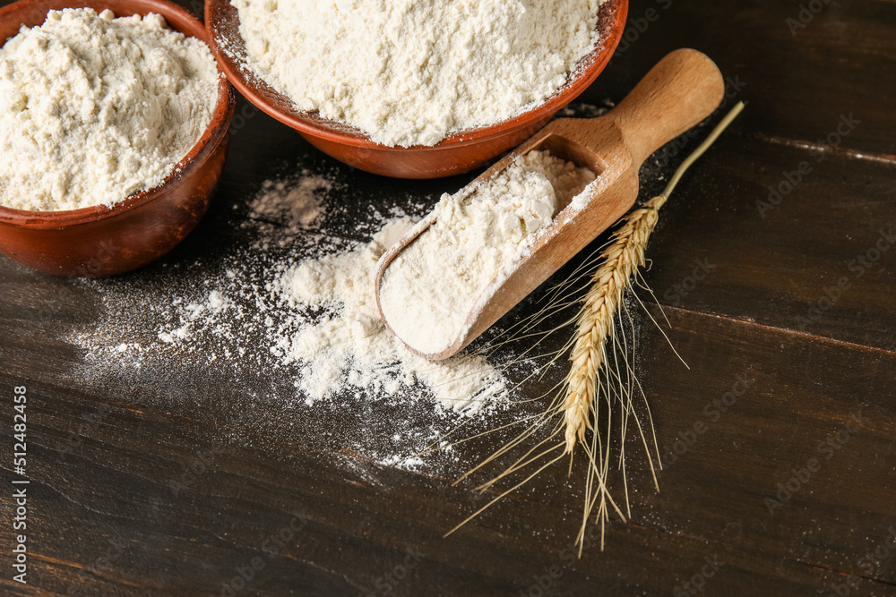 Scoop and bowls with wheat flour on dark wooden table