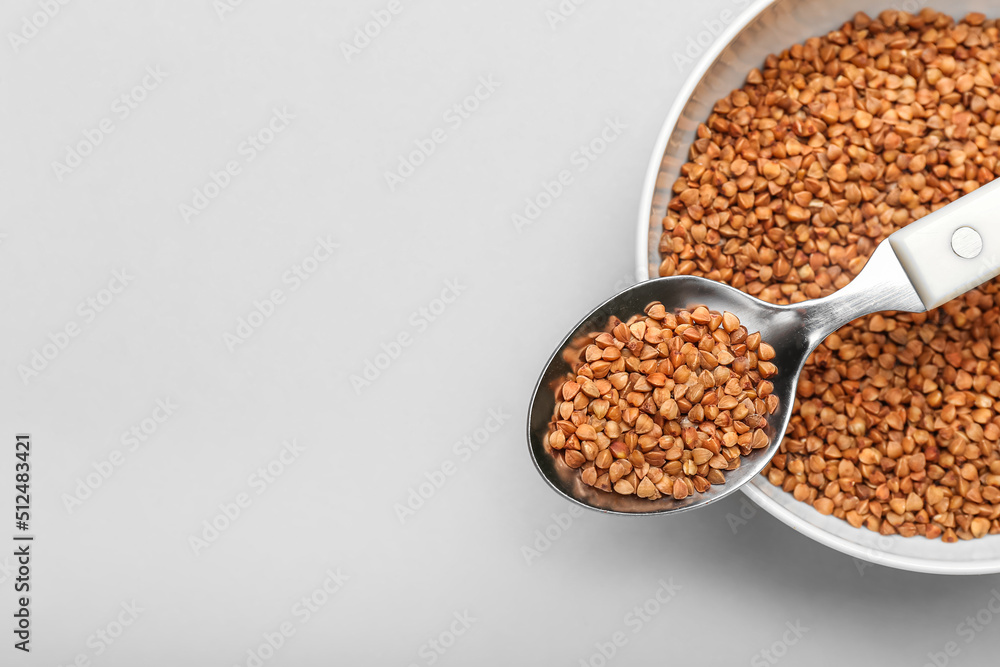 Bowl and spoon with buckwheat grains on light background, closeup