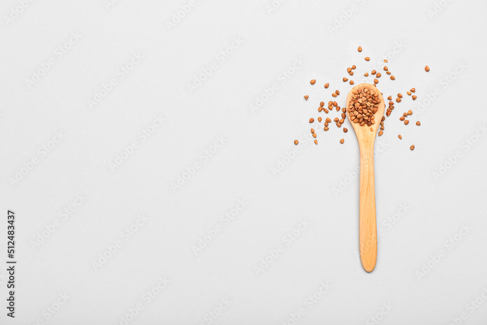 Wooden spoon with buckwheat grains on light background