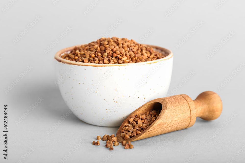 Ceramic bowl and wooden scoop with buckwheat grains on light background