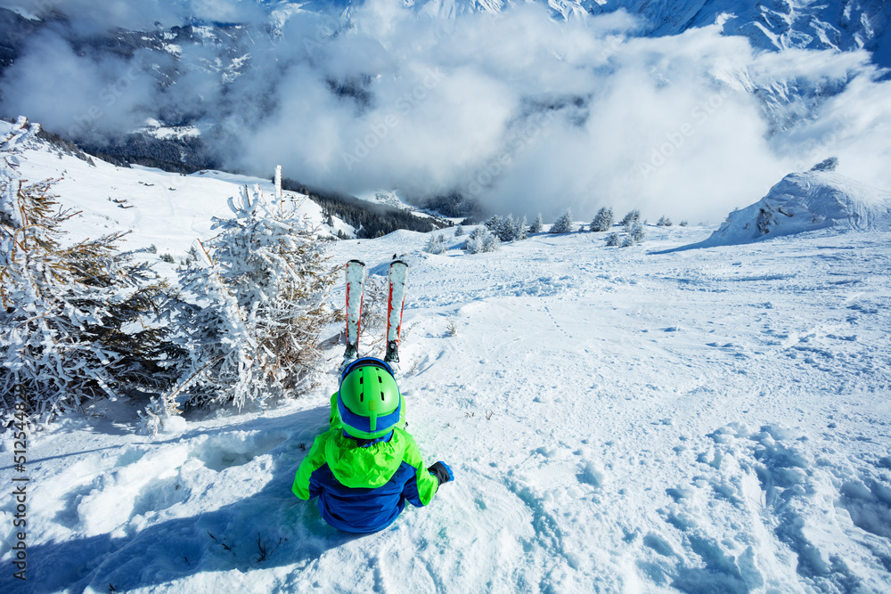 高山滑雪男孩坐在陡峭山坡上的雪地里