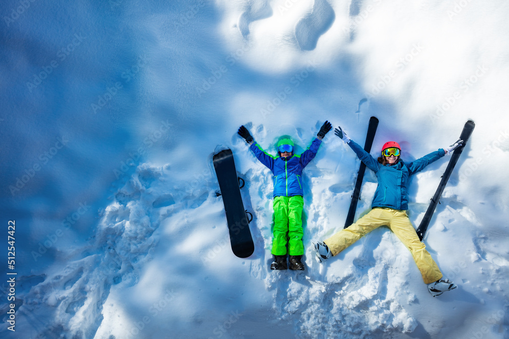 Mother and a boy lay in snow, wear ski outfit, view from above