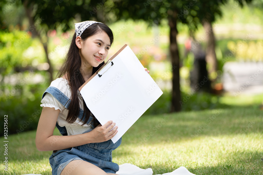 迷人的女孩，在阳光明媚的夏日，坐在公园的格子布上，用水彩完成