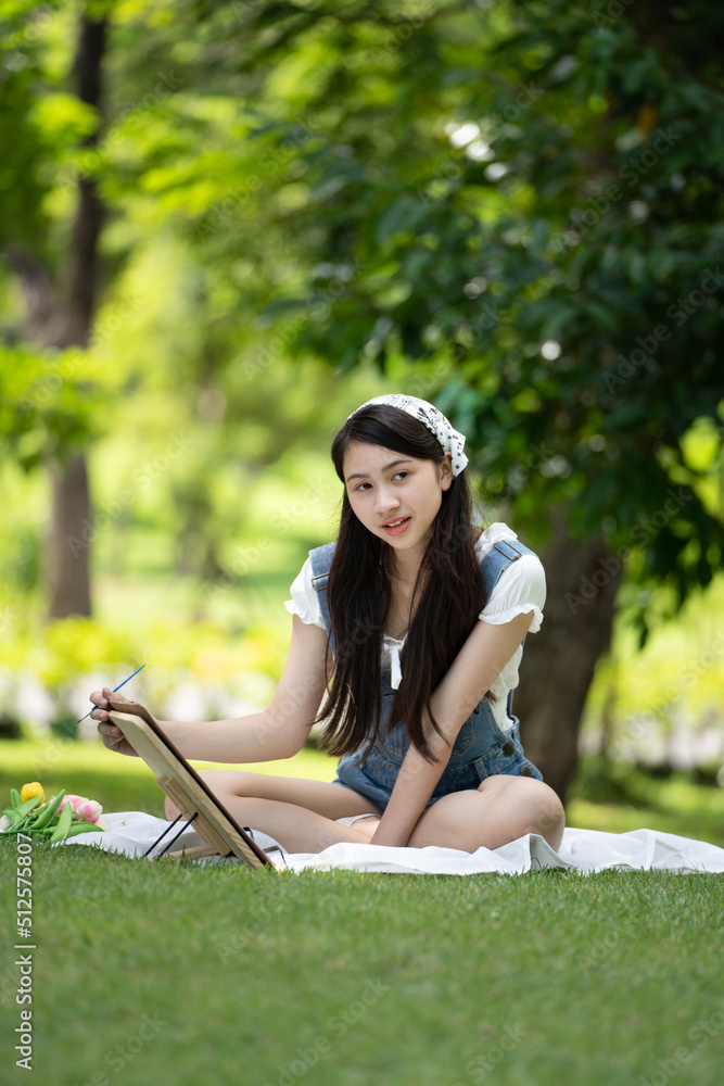 Charming Girl woman sitting on plaid at the park in sunny summer day and using watercolor for finish