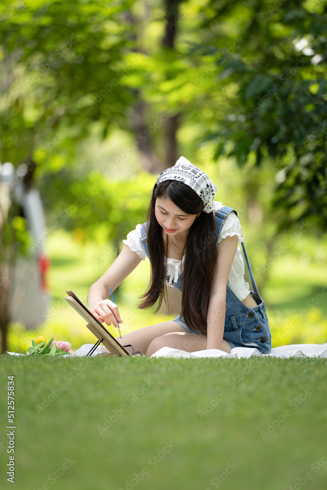 迷人的女孩，在阳光明媚的夏日，坐在公园的格子布上，用水彩完成