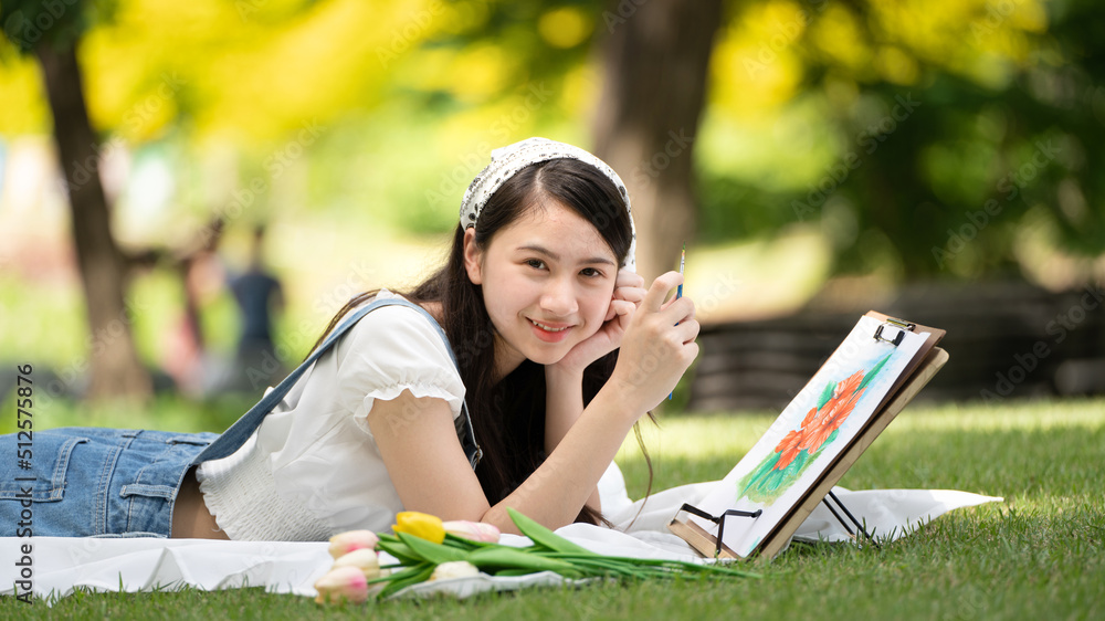 迷人的女孩，在阳光明媚的夏日，坐在公园的格子布上，用水彩完成