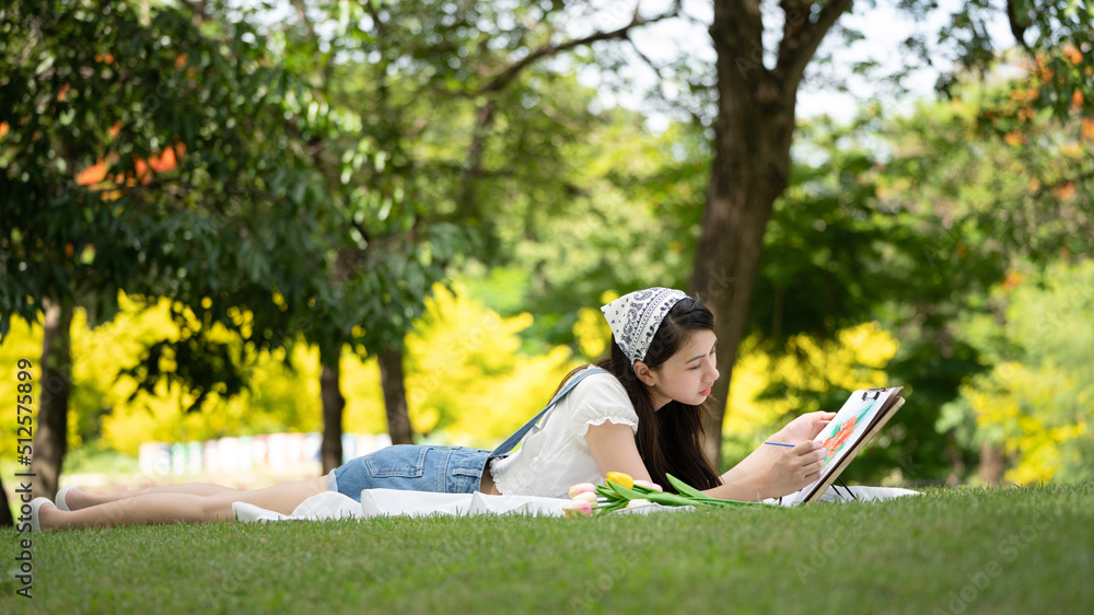 迷人的女孩，在阳光明媚的夏日，坐在公园的格子布上，用水彩完成