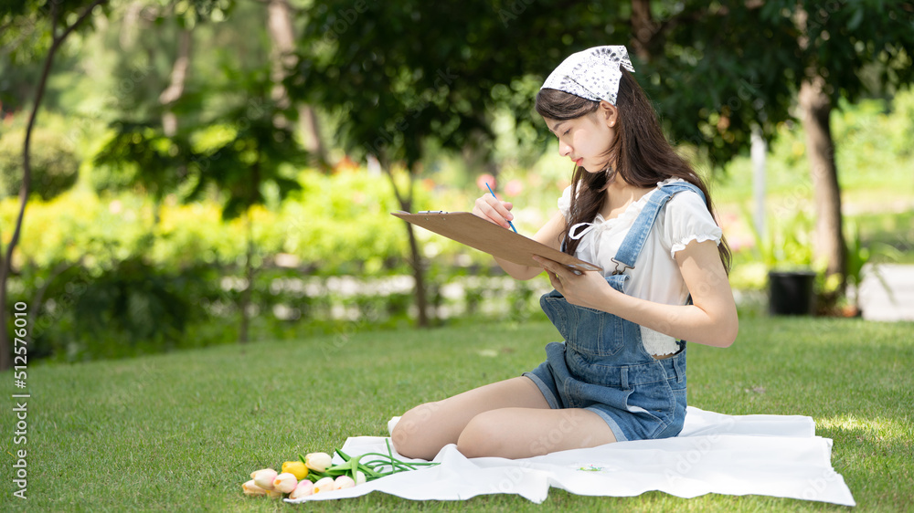 迷人的女孩，在阳光明媚的夏日，坐在公园的格子布上，用水彩完成