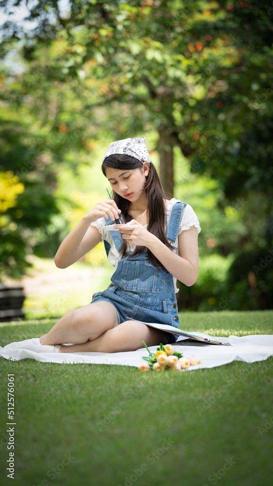 迷人的女孩，在阳光明媚的夏日，坐在公园的格子布上，用水彩完成