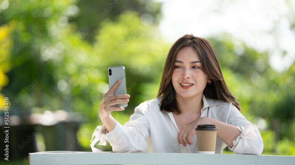 公园里使用智能手机的体贴微笑的女人，一位年轻迷人的商业女性的画像checki