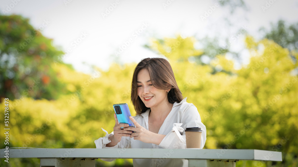 公园里使用智能手机的体贴微笑的女人，一位年轻迷人的商业女性的画像checki