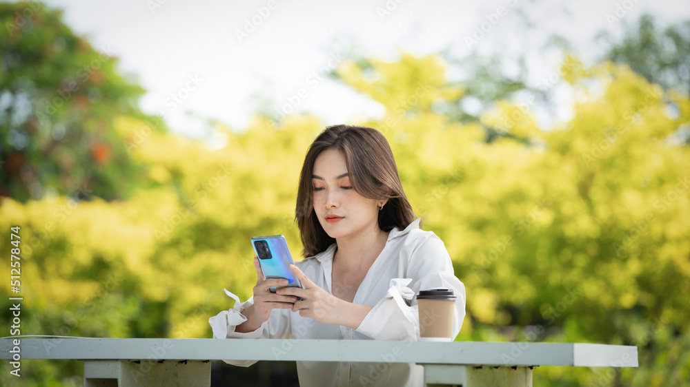 公园里使用智能手机的体贴微笑的女人，一位年轻迷人的商业女性的画像checki