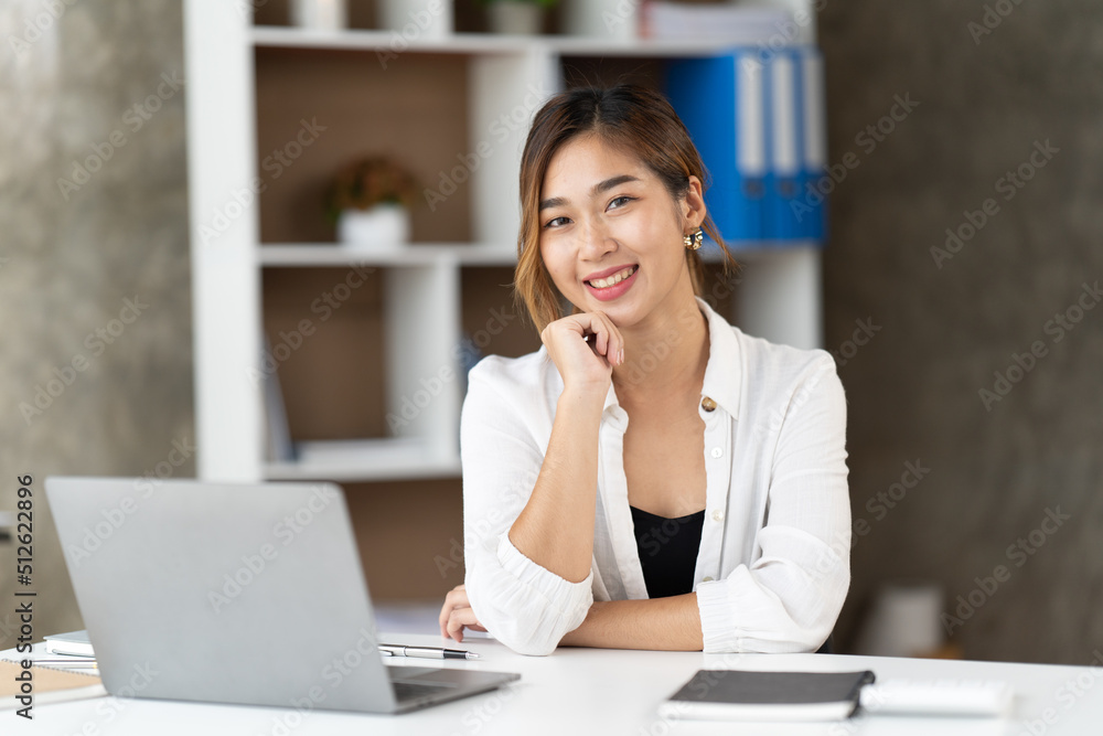 Beautiful young woman using laptop and smiling while working in office, business concept.