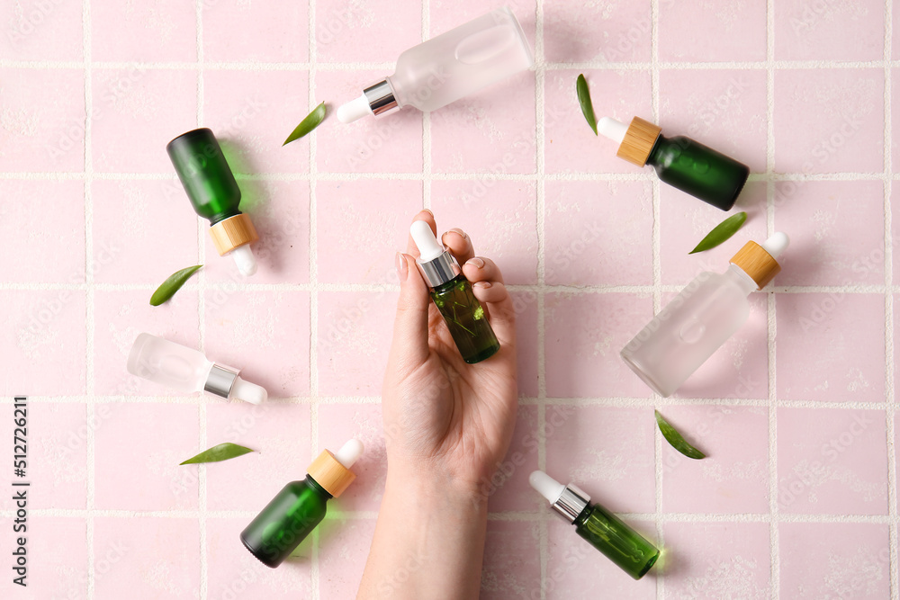 Female hand with different bottles of natural serum on color tile