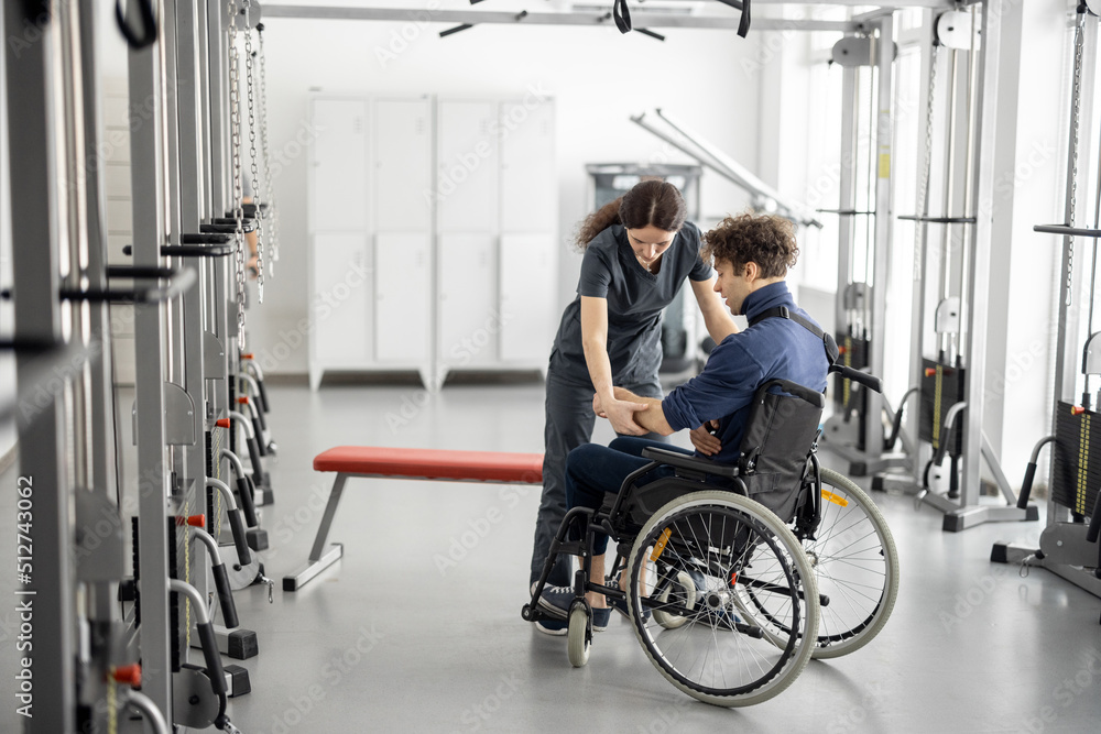 Rehabilitation specialist helps a guy stand out of a wheelchair at rehabilitation center. Concept of