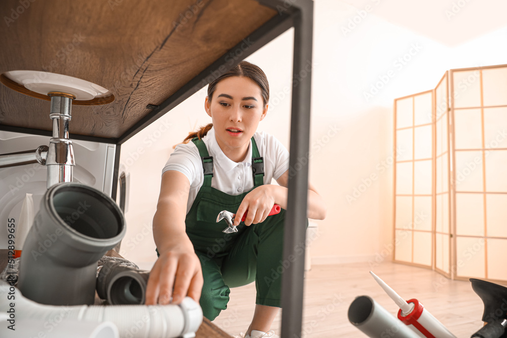 Asian female plumber with wrench near sink in bathroom