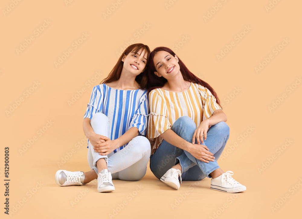 Teenage twin sisters sitting on beige background