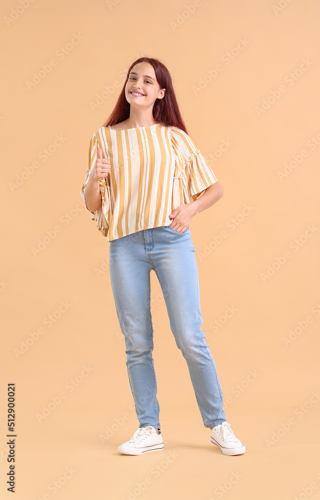 Teenage girl showing thumb-up on beige background