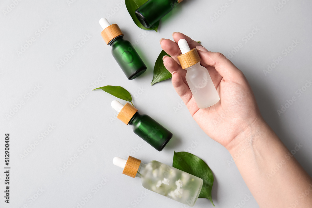 Female hand with bottles of natural serum and plant leaves on white background, closeup