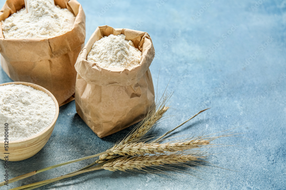 Wheat ears, paper bags and bowl with flour on blue background