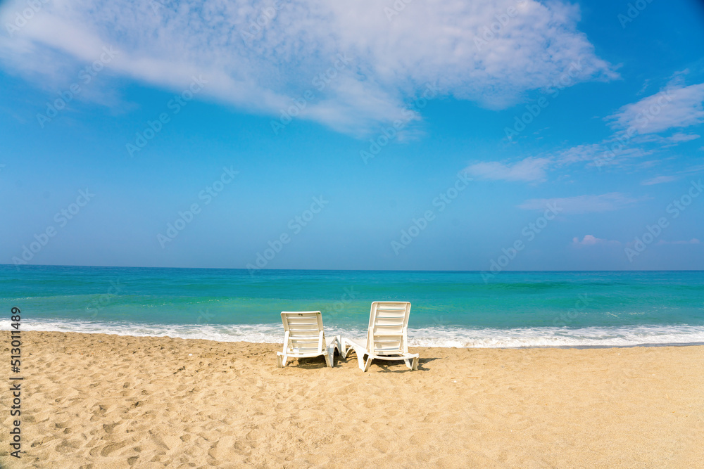 Two sun loungers on beautiful golden sandy beach against the backdrop of turquoise sea and blue sky 