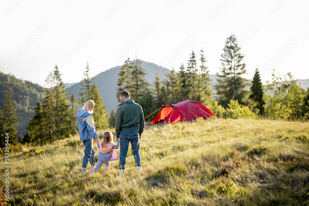 年轻的高加索家庭带着小女孩一起在绿色草地上行走，带着帐篷旅行