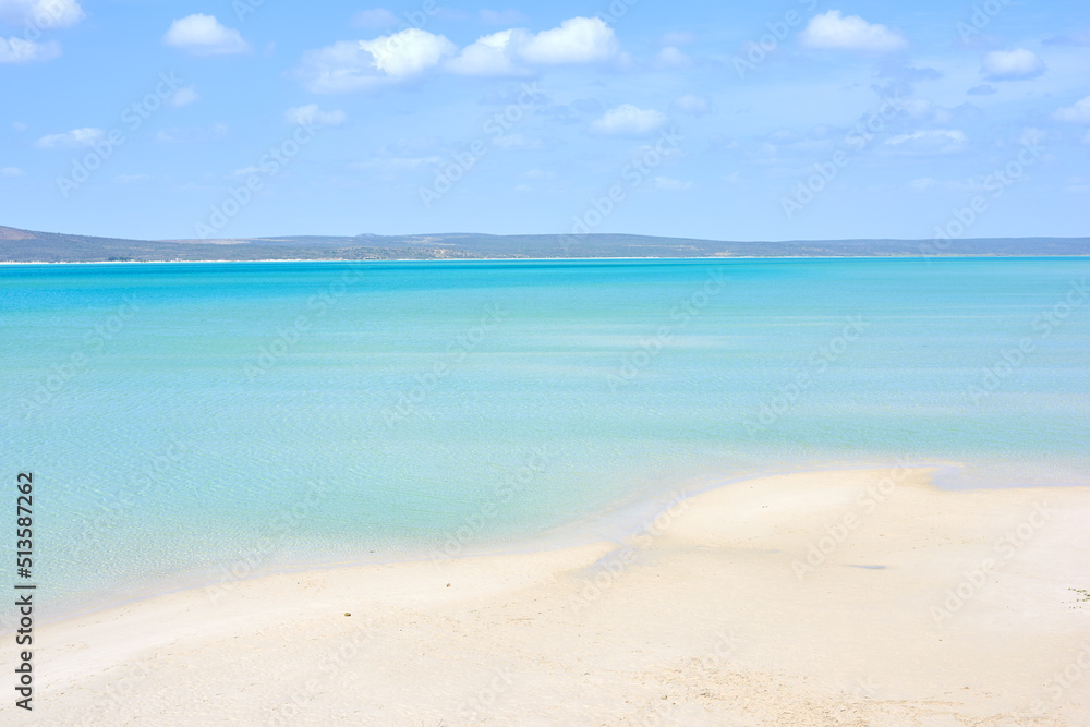 A clear beach during summer with a cloudy sky. Blue ocean water at the seashore on a hot day. Beauti