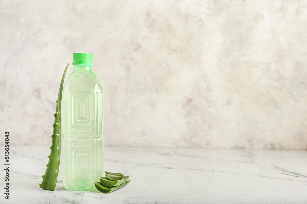 Bottle of aloe juice and leaves on light background