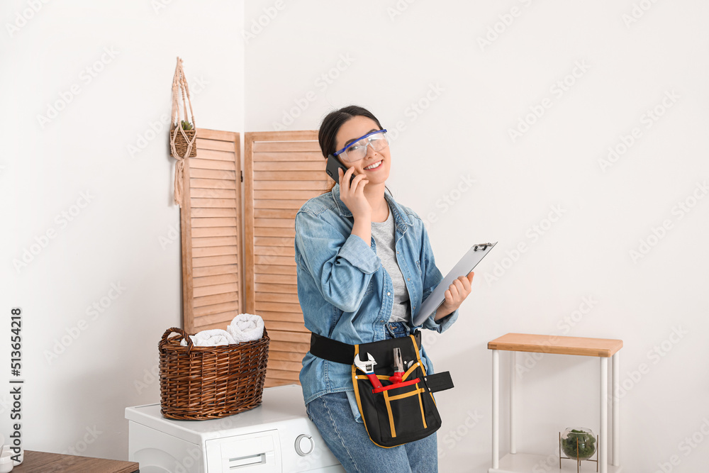 Asian female plumber with clipboard talking by mobile phone in bathroom