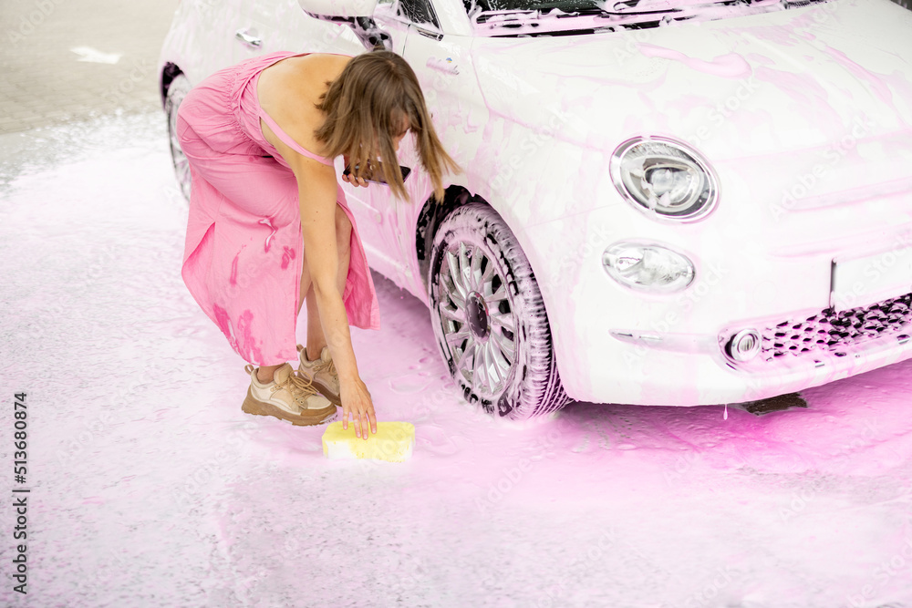 Woman stands in pink foam while washing her vehicle at car wash. Glamorous car wash process