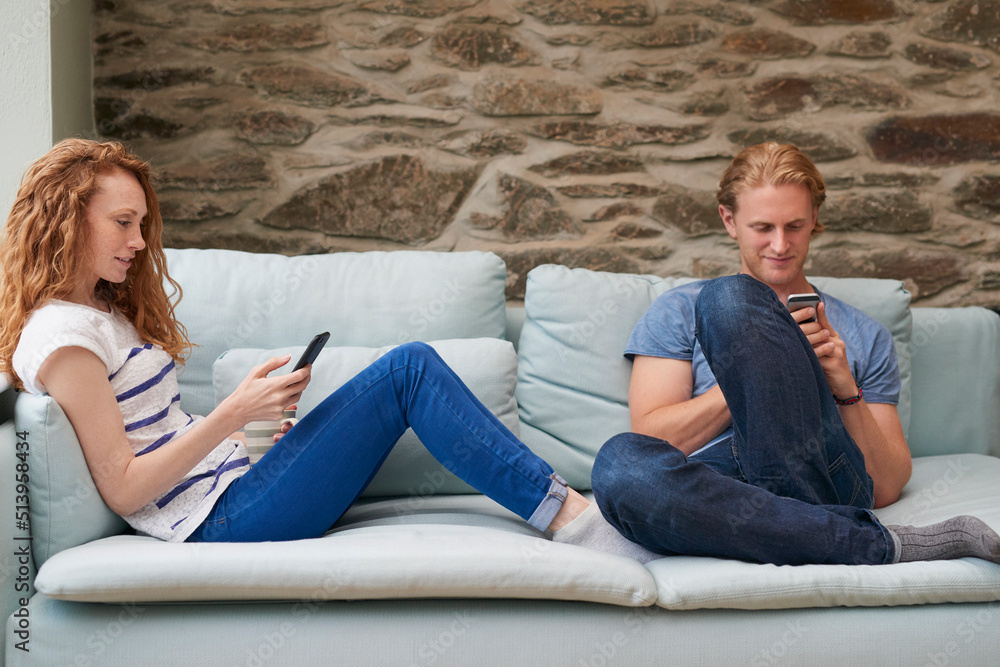 A young couple using smartphones while spending time together at home