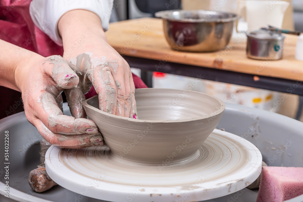 Hands of a potter on a pottery wheel close-up making flat and wide plate. Old traditional art, handm