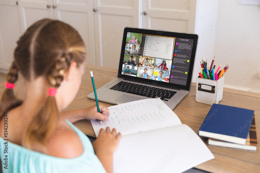 Caucasian girl writing notes in book given during online lecture over video call on laptop at home