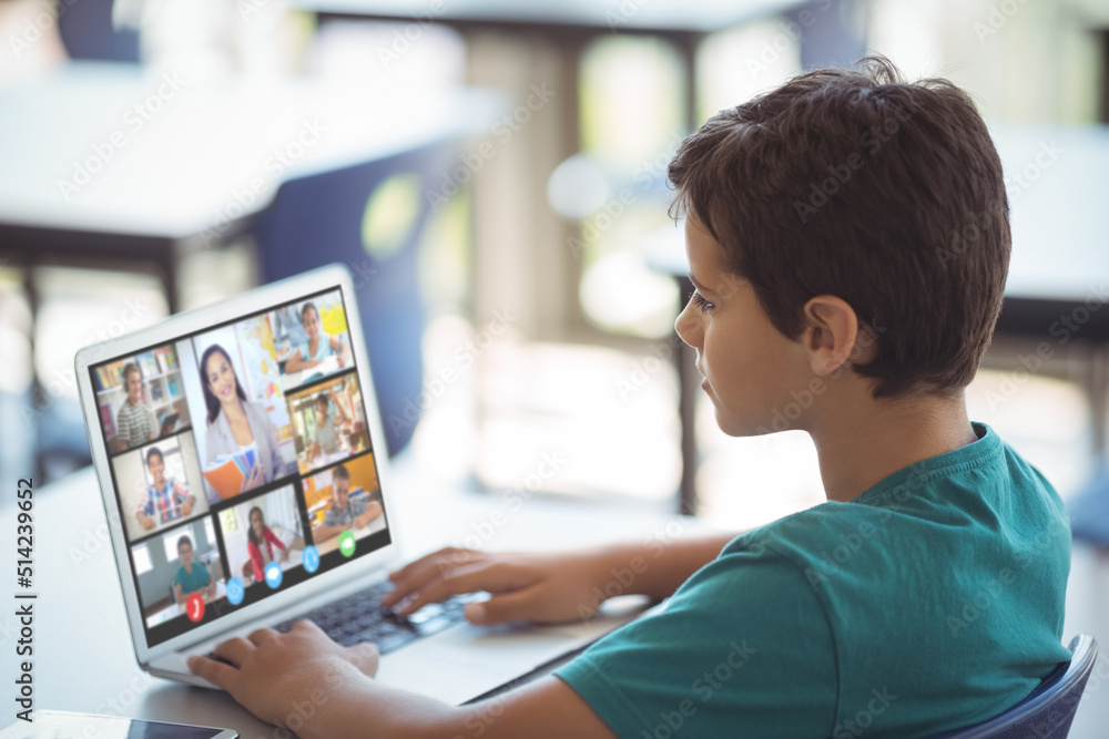 Focused caucasian boy looking at screen while attending online class over laptop on table at home