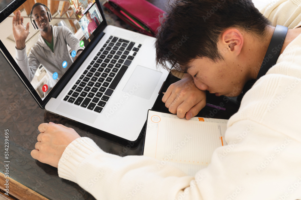 Bored asian teenage boy sleeping in front of laptop during online lecture on table at home