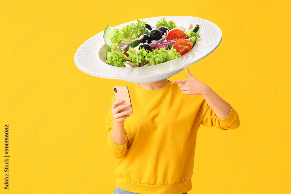 Woman with phone and plate of tasty Caesar salad instead of her head on yellow background