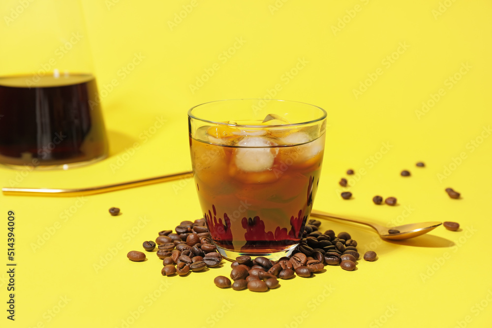 Glass with cold brew and coffee beans on yellow background