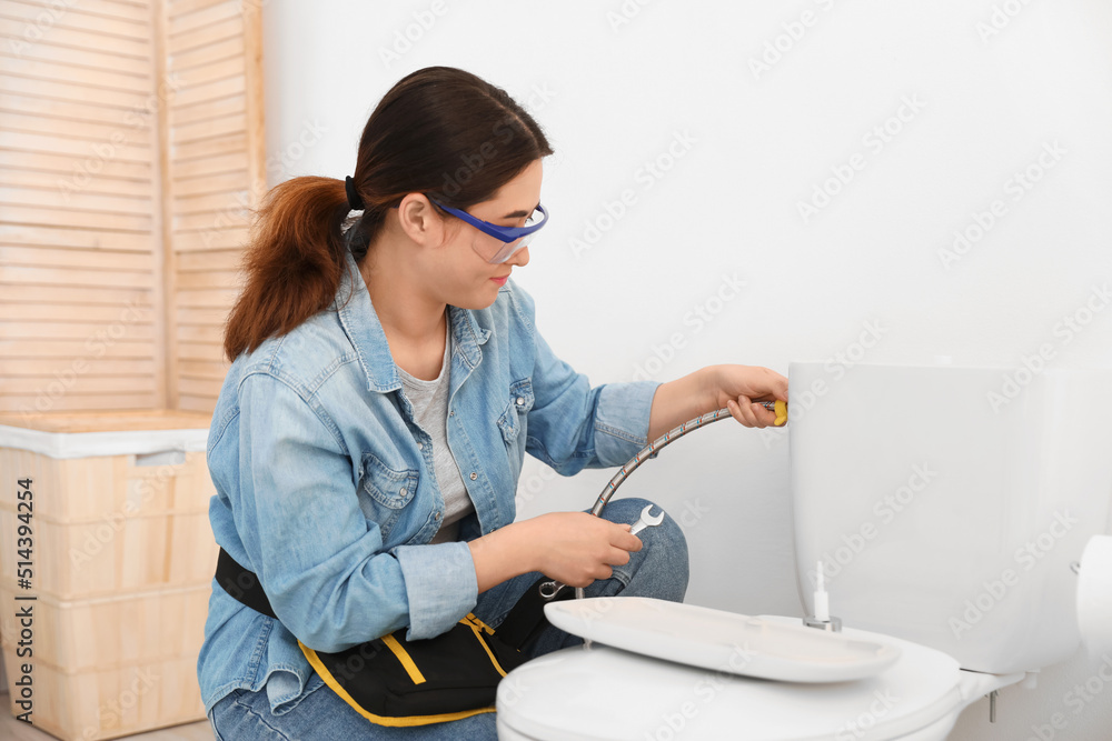 Asian female plumber fixing toilet bowl in bathroom