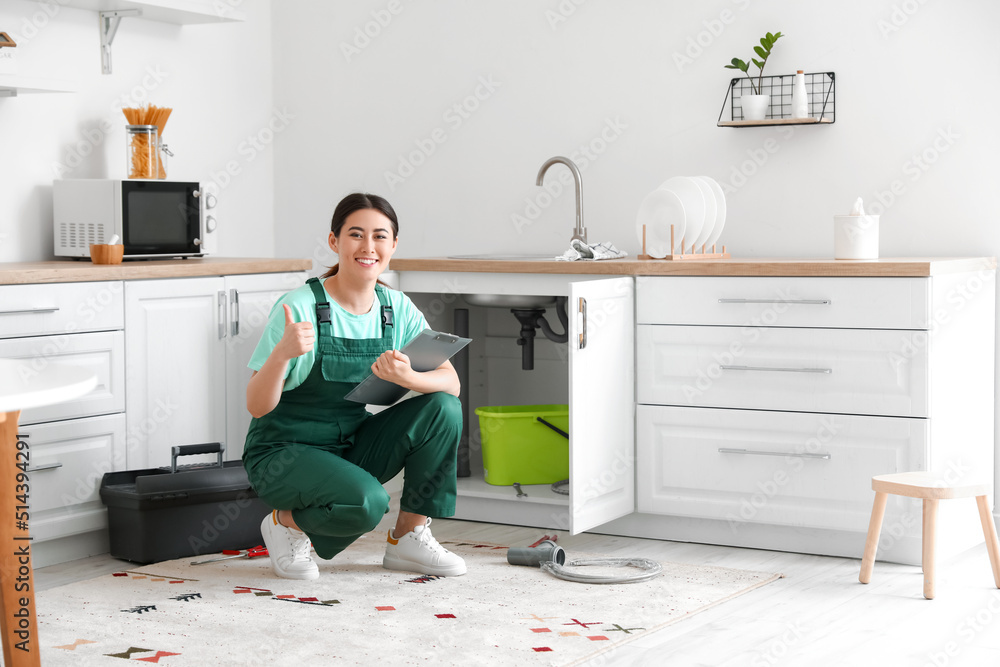 Asian female plumber with clipboard showing thumb-up in kitchen