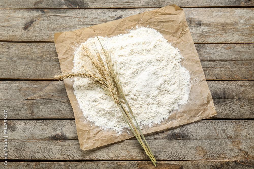 Parchment paper with wheat ears and flour on wooden background