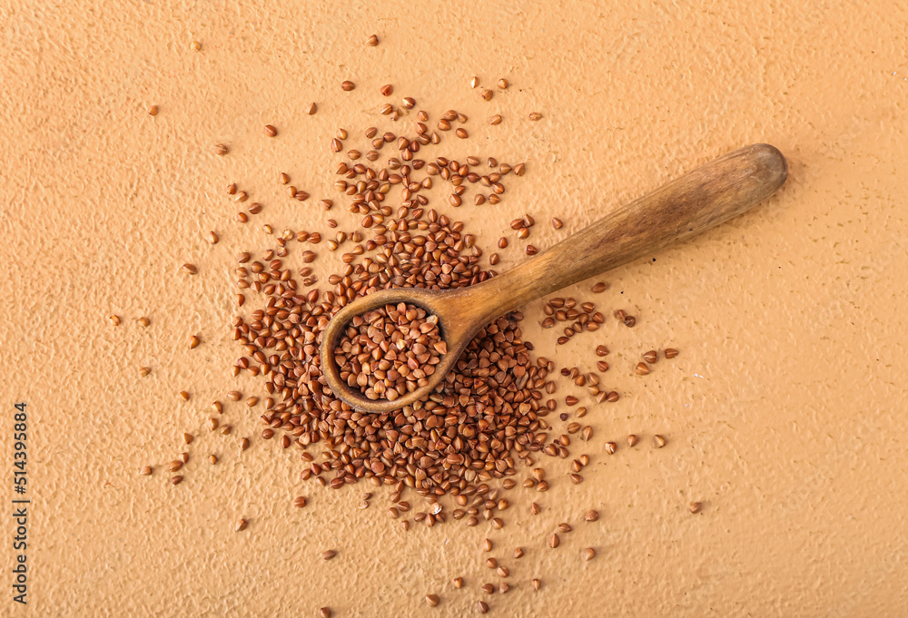 Wooden spoon and scattered buckwheat grains on color background