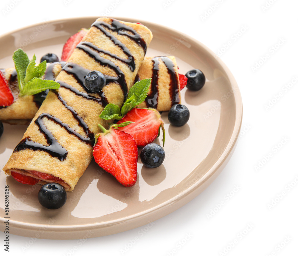 Plate of thin pancakes with strawberries, chocolate syrup and mint leaves on white background