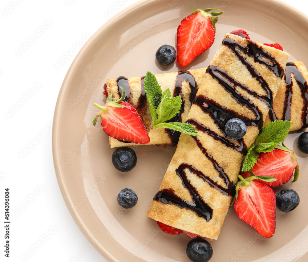 Plate of thin pancakes with strawberries, chocolate syrup and mint leaves on white background