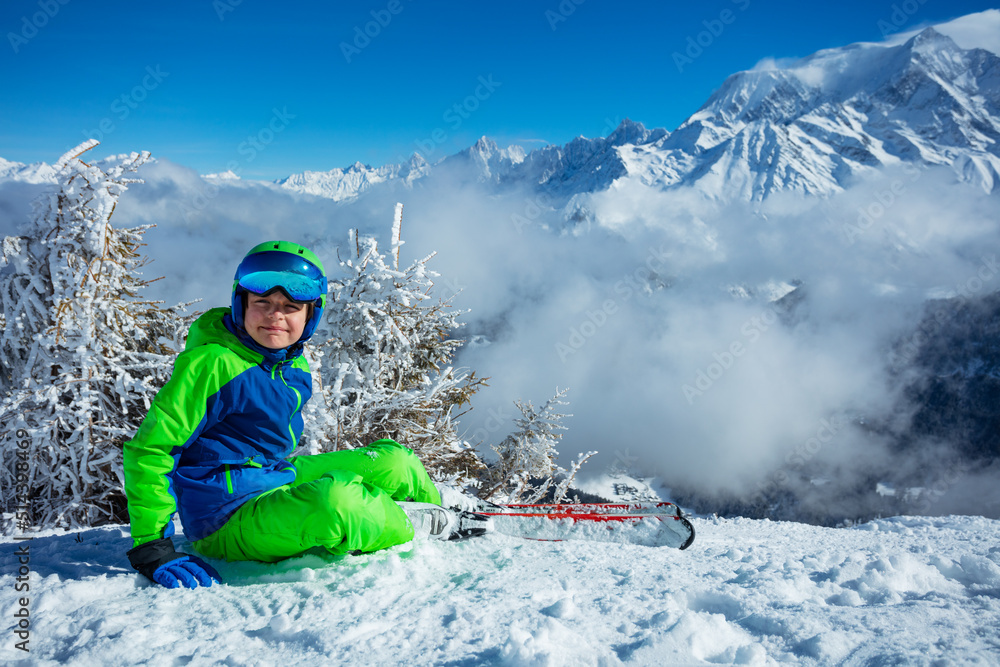 滑雪男孩微笑着坐在云雾覆盖的山顶上