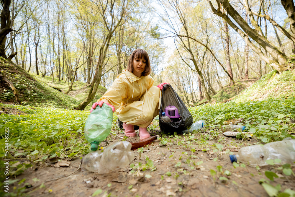 Young woman in protective clothes collecting scattered plastic garbage in the woods. Problem of bed 