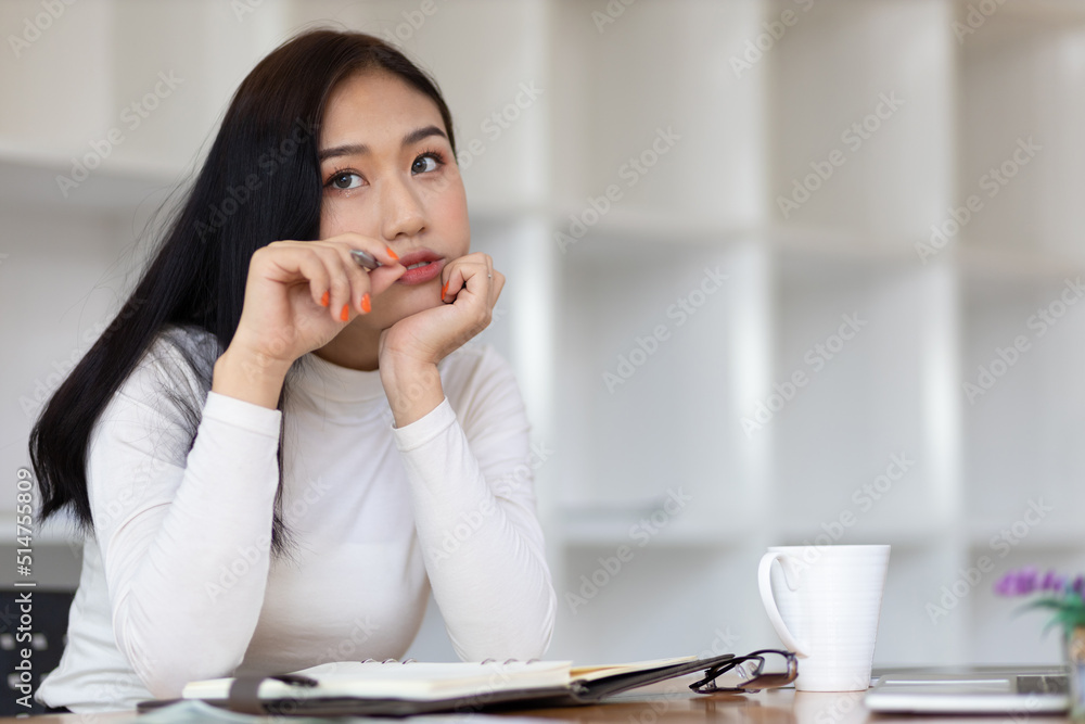 Beautiful Asian woman in the home office thinking and writing a schedule on a notepad.