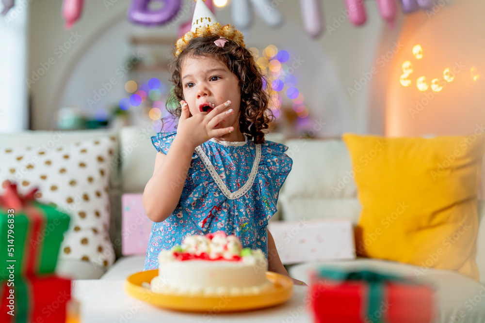 生日快乐，穿着周年纪念服，戴着派对帽的小女儿为h享用手指美味的甜蛋糕