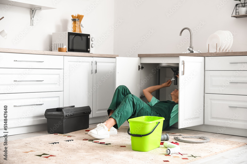 Female plumber fixing sink in kitchen