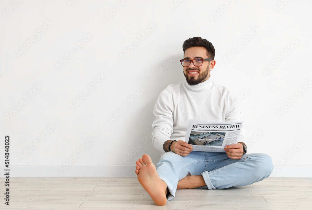 Handsome barefoot man reading newspaper near light wall