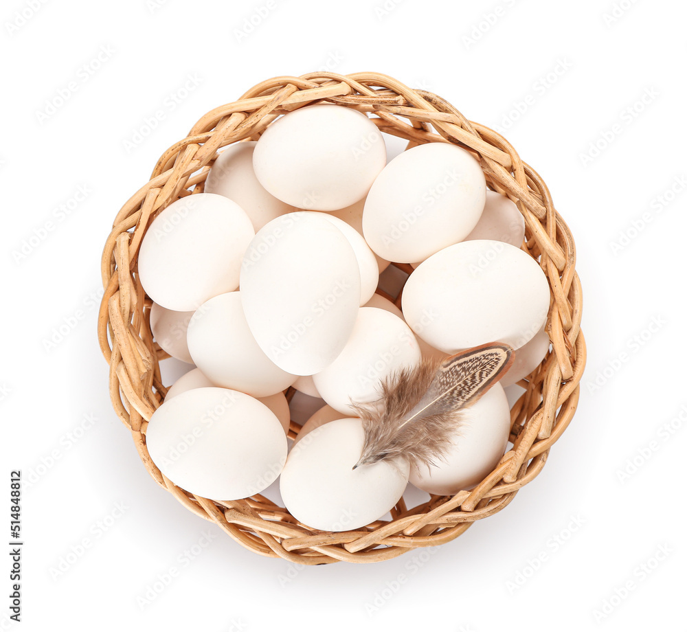 Wicker basket with chicken eggs and feather on white background